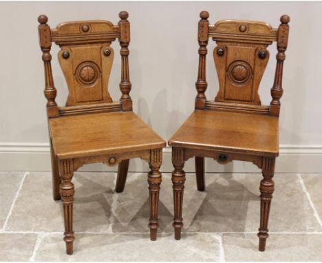 A pair of Victorian Aesthetic Movement honey oak hall chairs, each chair with button finials above a shaped splat centred wit