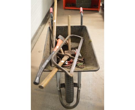 A modern wheelbarrow containing several hand tools, comprising: an axe, hedge knife, hammer, saw, etc.