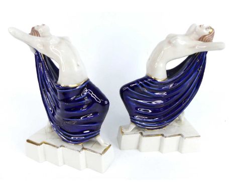 A pair of Art Deco glazed ceramic semi-nude figures by Royal Dux, each modelled in outstretched standing pose holding a blue 