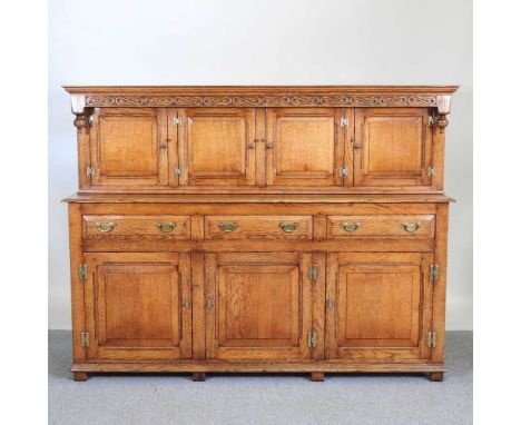 A good quality 17th century style light oak court cupboard, 20th century, having a carved frieze, over panelled doors and dra