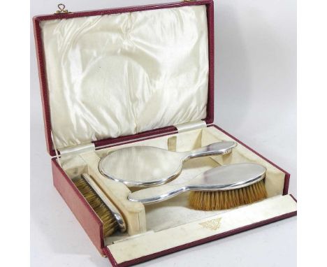 An early 20th century silver three piece vanity set, comprising a hand mirror and two brushes, Birmingham 1913, in a fitted c