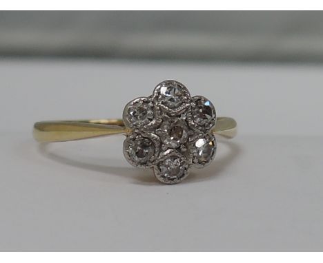 A ladies diamond daisy cluster ring having a milligrain setting on a yellow metal loop stamped 18