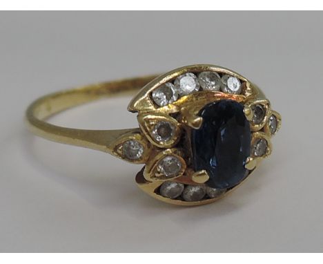 A ladies dress ring having an oval sapphire within a decorative diamond surround on a yellow metal loop stamped 18ct