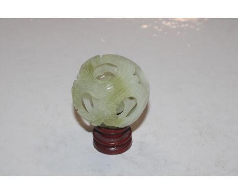 A carved jade coloured puzzle ball on wooden stand 