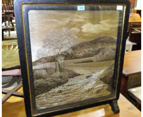 A Victorian ebonised firescreen, finely embroidered with a river scene