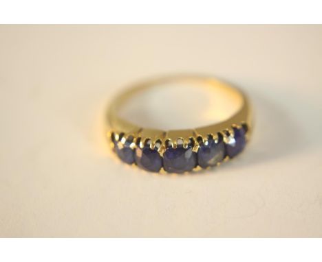 A yellow metal (tests higher than 9ct) sapphire carved half hoop ring. Set with five cushion shaped mixed cut sapphires with 