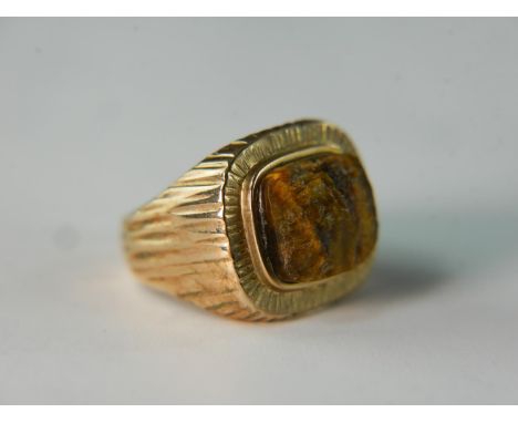 A textured bark effect 9 carat yellow gold signet ring, inset with a rough cut tigers eye. Ring size R, 14.9g gross weight. 