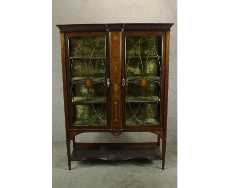 An Edwardian inlaid mahogany twin door display cabinet, the cornice carved with stylised flowers and with shaped shelf undert