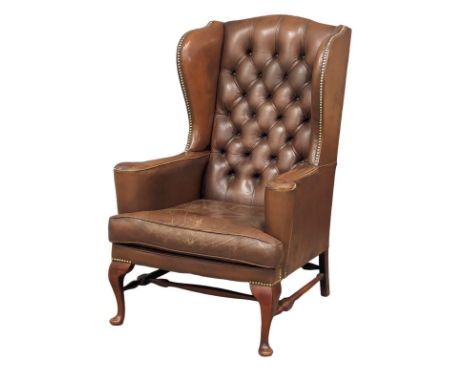 A brown deep button back leather wingback armchair in the early Georgian style 