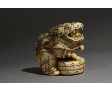 A late 18th century Japanese netsuke from Edo period. Not signed. In carved elephant tusk portraying a child wearing a Shishi