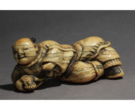 An 18th century Japanese netsuke from Edo period. In carved elephant tusk and horn portraying a Karako lying on the floor wit