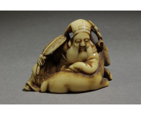 A 19th century Japanese netsuke from Edo period. Signed Tomochika on the base. In carved elephant tusk portraying a sat Juroj