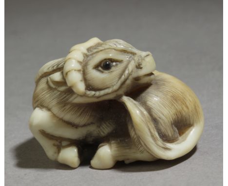 A 19th century Japanese netsuke. Signed Tomozan on the base. In carved elephant tusk and horn eyes portraying a recumbent Kir