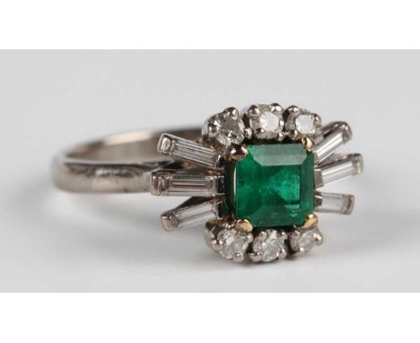 A white gold, emerald and diamond ring, claw set with a rectangular step cut emerald between baguette cut diamond three stone