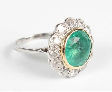 A gold, platinum, emerald and diamond circular cluster ring, collet set with the large circular cut emerald within a surround