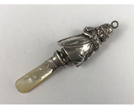 A George V baby's silver soother / rattle, modelled as a little girl holding a sprig of flowers, on a mother of pearl handle,