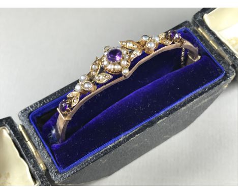 A Belle Epoque amethyst and pearl hinged bangle, having an open lenticular face surmounted by millegrain and pave set blossom