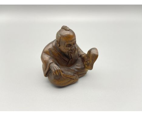 A Hand carved Japanese netsuke of an elderly gentleman sitting holding a mask. Signed by the artist. [As found] [3.5cm height