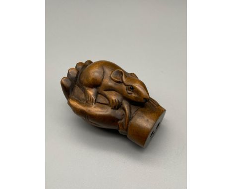 A Japanese hand carved netsuke of a mouse within a hand. Signed by the artist. Mouse is detailed with black bead eyes. [5cm l