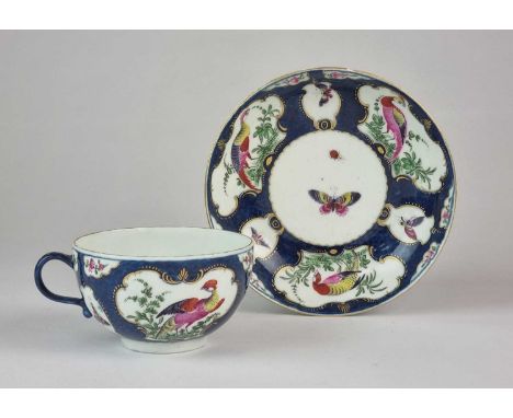 A Worcester teacup and saucer, circa 1775, painted with exotic birds and butterflies in scrolling cartouches against a scale 