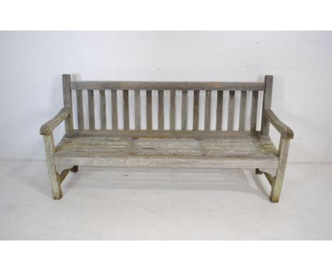 A weathered wooden garden bench with slatted seat - length 180cm