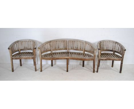 A weathered curved wooden garden bench with two matching chairs
