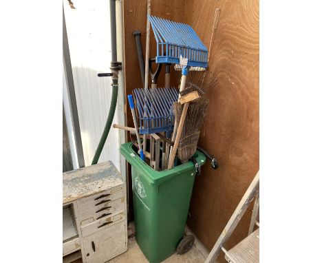 A WHEELIE BIN CONTAINING AN ASSORTMENT OF GARDEN TOOLS TO INCLUDE FORKS AND RAKES ETC 
