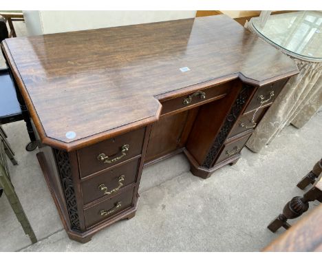 AN EDWARDIAN MAHOGANY BREAKFRONT KNEEHOLE DESK WITH SEVEN DRAWERS, CENTRAL CUPBOARD AND CHIPPENDALE STYLE PANELS 