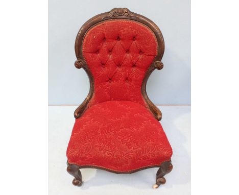 A Victorian walnut spoon back nursing chair with button back, red floral fabric upholstery and frilled gimp, raised on cabrio