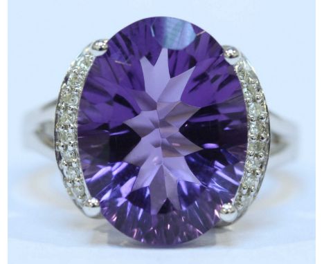 A 9ct white gold amethyst and diamond ring, claw set with a large central, oval amethyst, the mount flanked on either side by