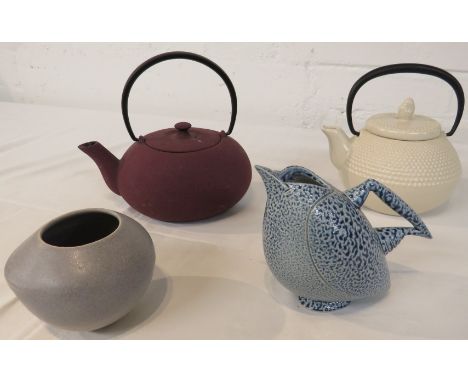 A metal teapot in a purple anodized finish, a cream ceramic teapot with black metal handle, a studio pottery jug modelled as 