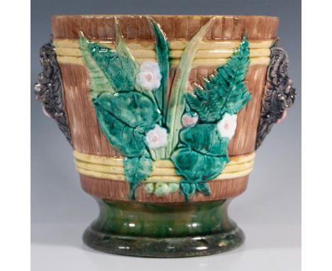 A large bucket-shaped planter adorned with figural handles on either side and bas-relief botanical features between them. Han