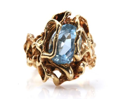 An American blue topaz ring, c.1970,with an oval mixed cut blue topaz, set to a looped molten effect mount and shank. Marked 