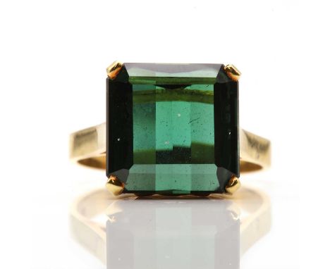 A single stone tourmaline ring,with a modified trap cut green tourmaline, four claw set to a pierced collet, with open should