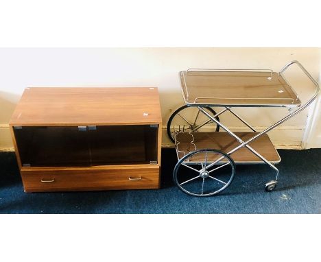 A 1970's teak glazed display shelf unit, fitted with a single drawer and brass handles; a similar chrome frame tea trolley. (