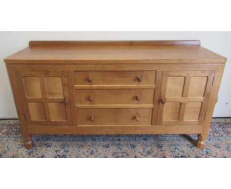 Robert Mouseman Thompson of Kilburn - a panelled oak sideboard with adzed top above three drawers enclosed by two four panel 