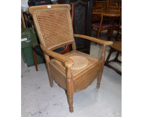 An Edwardian commode armchair with cane seat and back, original pot