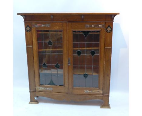An Art and Crafts oak book case with two leaded glass doors enclosing adjustable shelves and raised on carved bracket feet, H