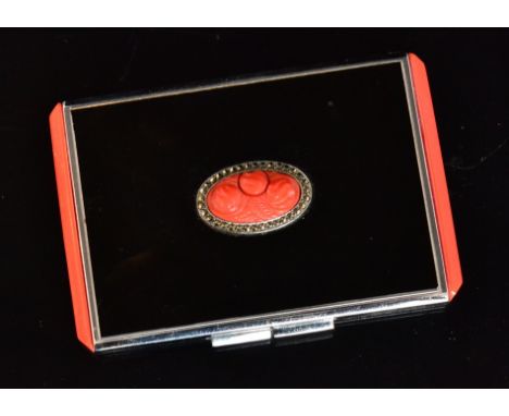 Unknown - An Art Deco black enamel and marcasite compact of rectangular outline, the hinged lid centred by a carved coral col