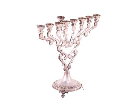 A Hanukkah menorah, a candelabrum with nine branches, in scrolled design, supported on three bracket feet, white metal stampe