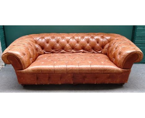 A brown leather button upholstered Chesterfield sofa, with roll-over arms on turned supports, 198cm wide x 70cm high x 95cm d