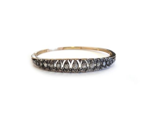 A gold and silver fronted, diamond set oval hinged bangle, mounted with a row fo cushion shaped diamonds, in lozenge shaped s