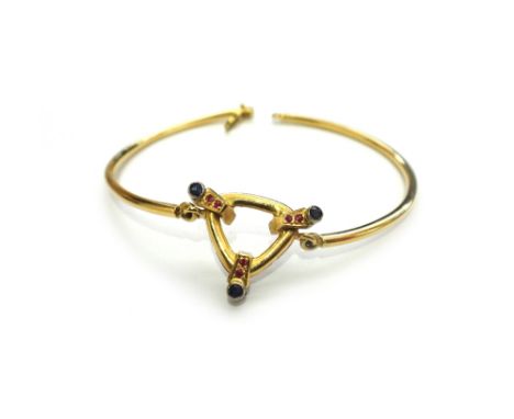 A gold, sapphire and red gem set bracelet, formed as two semi-circular bars, with an openwork gemstone set trefoil shaped mot