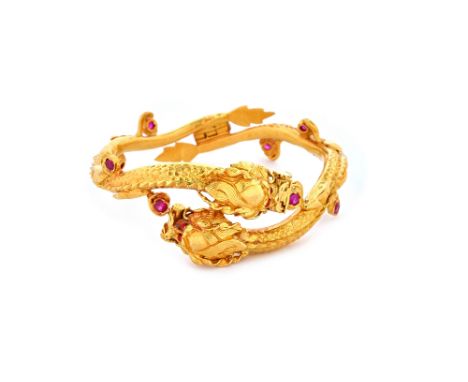 An Indian gold and red gem set hinged bangle designed as two undulating intertwined dragons.   Illustrated