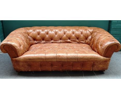 A brown leather button upholstered Chesterfield sofa, with roll-over arms on turned supports, 198cm wide x 70cm high x 95cm d