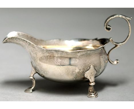 A GEORGE II SILVER CREAM BOAT, WITH LEAF CAPPED FLYING SCROLL HANDLE, ON THREE HOOF FEET, 12CM L, MAKER'S MARK RUBBED, LONDON