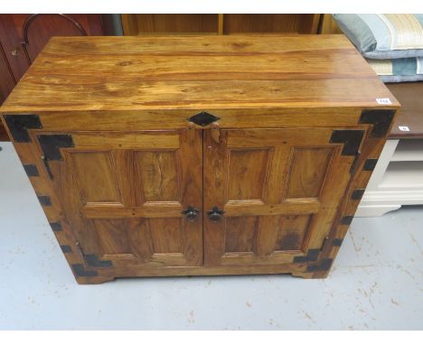 A contemporary Indian style oak cupboard with metal fittings, two doors and a single shelf within, approximately 91 cm wide, 