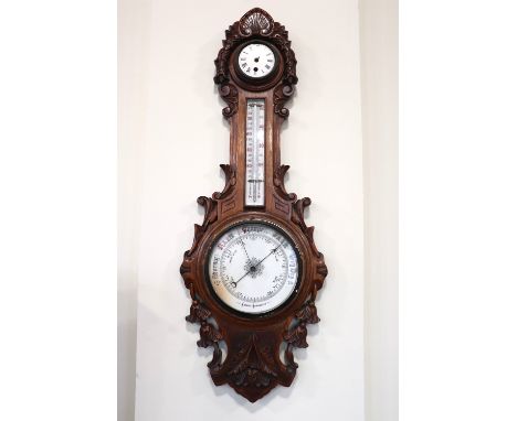 A Victorian carved oak banjo barometer / clock, comprising an aneroid barometer and a thermometer, surmounted by a clock, hav