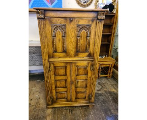 A distressed oak cocktail cabinet with raised panelled sides and lower doors, arch panel carved fall front with mirror interi