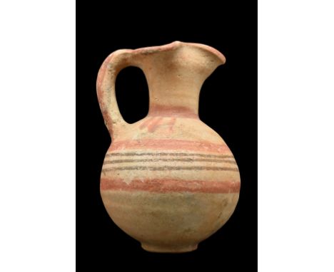 Ca. 1050-750 BC.A bichrome pottery jug with a globular lower body, flattened base, and sturdy handle. The trefoil-shaped spou